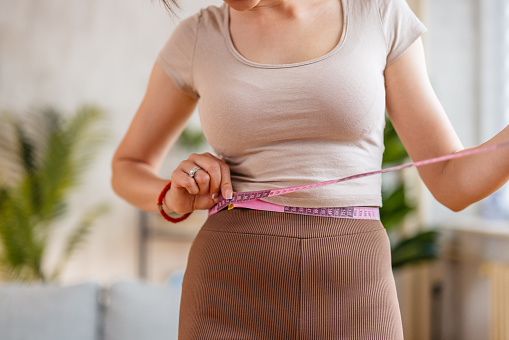 Mujer joven midiendo su cintura en casa photo