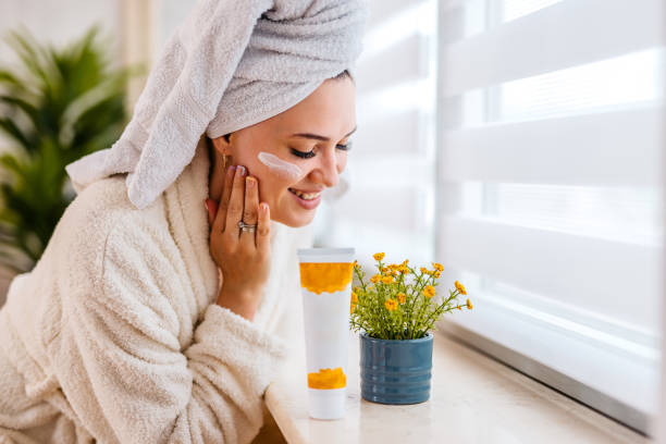 istock Young Woman With A Moisturizer On Her Face Standing Next To A Window At Home 1560418225