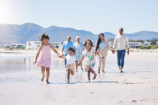 Beach, big family and children holding hands, running and happiness on summer vacation together in Mexico. Sunshine, fun and bonding, men, women and kids on holiday walk on happy morning with energy.