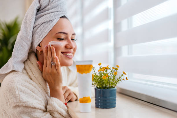 istock Young Woman With A Moisturizer On Her Face Standing Next To A Window At Home 1560428807