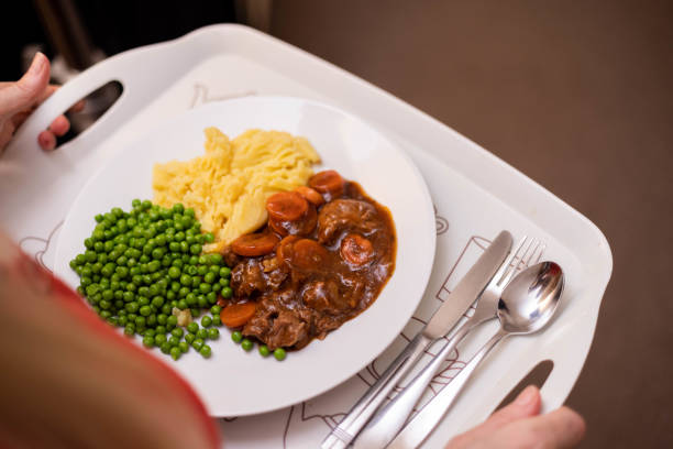 A close up elevated view of an unrecognisable community nurse visiting a patient in their home in Northumberland, England. She is holding a hot meal of steak, carrots, peas and mashed potato on a dinner tray.