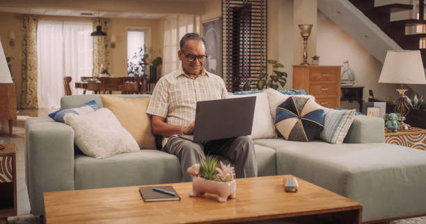 istock Elderly Indian Man Using Laptop at Home: Using Online Platforms to Explore His Interests, Delving into History, Arts, and Literature. Cultivating Wisdom and Sharing Stories On Social Media. 1560454936