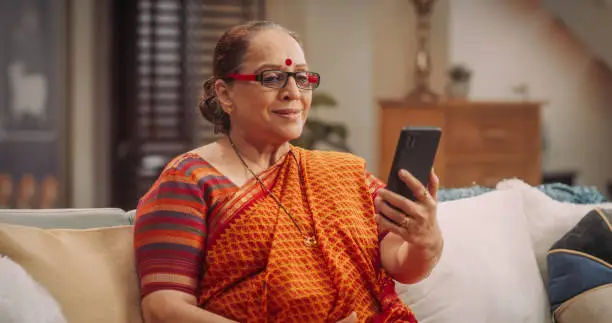 Elderly Indian Woman Using Video Call on Smartphone: Talking Long-Distance Friends, Smiling. Joyful Smiling Senior Lady Talking to Her Family, Relatives, Grandchildren. Closeup
