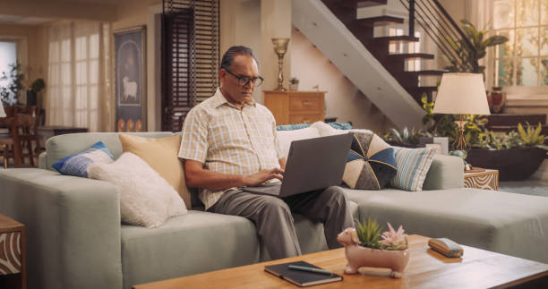 istock Elderly Indian Man Using Laptop at Home: Using Online Platforms to Explore His Interests, Delving into History, Arts, and Literature. Cultivating Wisdom and Sharing Stories On Social Media. 1560475742