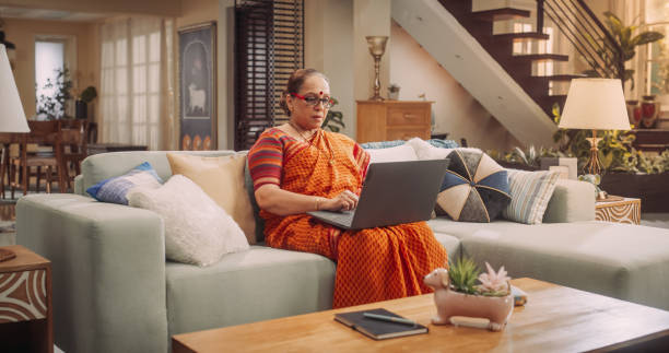 istock Elderly Woman Using Laptop at Home: Using Internet, Connecting with Loved Ones On Social Media, Exploring New Interests. Beautiful Grandmother Adapting to Technology with Grace, Curiosity. 1560476819
