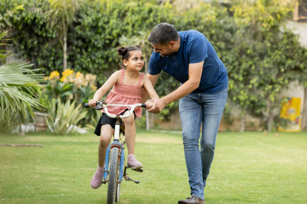 istock Indian father teaching riding a cycle to his daughter in lawn 1560480547