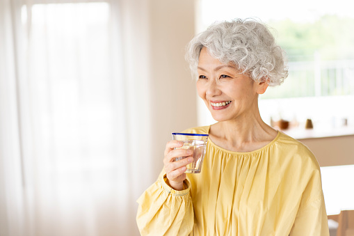 Portrait of a smiling Japanese senior woman holding a glass of water.Heatstroke measures. Health beauty.