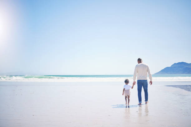 istock Father, boy and beach with mockup space, holding hands and blue sky with bonding with vacation in summer. Papa, male kid and solidarity with trust, holiday and ocean mock up with waves in sunshine 1560486322