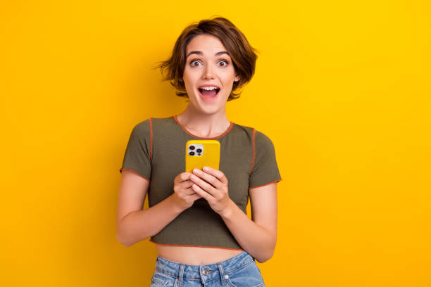 Photo of impressed girl with bob hairstyle dressed khaki t-shirt hold smartphone astonished staring isolated on yellow color background Photo of impressed girl with bob hairstyle dressed khaki t-shirt hold smartphone astonished staring isolated on yellow color background. excited woman yellow stock pictures, royalty-free photos & images