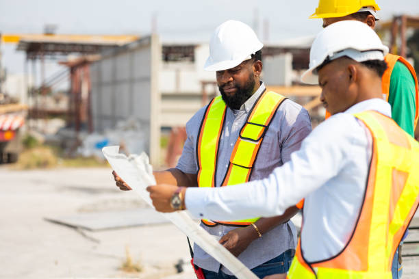 istock Happy Engineering worker in safety hardhat and architect looking at blueprint at industrial Heavy Manufacturing Factory. Prefabricated concrete walls. Professional Engineer Team working 1560514344