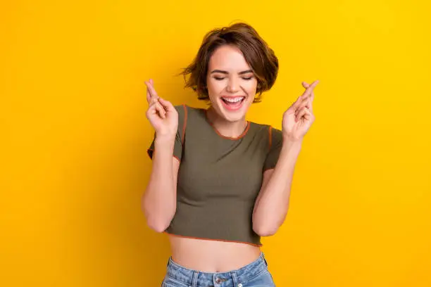 Photo of Photo of good mood adorable girl dressed stylish khaki t-shirt making wish laughing eyes closed isolated on yellow color background