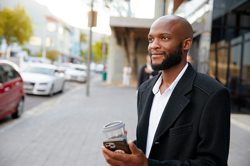 Closeup of a businessman on the go in the city, holding his phone and a cup of coffee