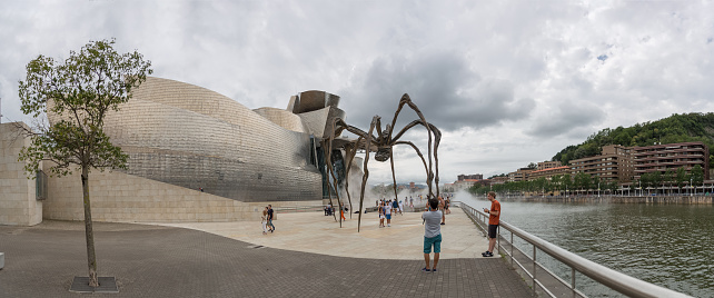 Bilbao Spain - 07 05 2021: Panoramic exterior view at the iconic Guggenheim Museum Bilbao, Maman spider sculpture, iconic museum of modern and contemporary art, Nervion river and Bilbao downtown city