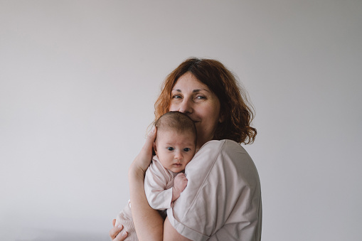 Portrait of happy mum holding infant child on hands. Loving mom carying of her newborn baby at home. Mother hugging her little 1 months old girl.