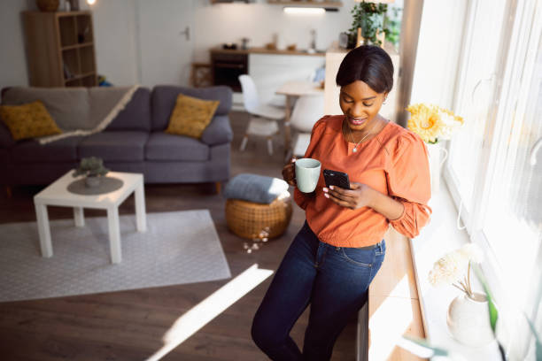istock Young woman of Black ethnicity, using mobile phone while holding coffee 1560561432