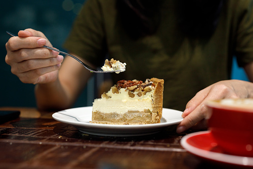 A close-up image of a young woman enjoying a delicious cheesecake and coffee in a cafe