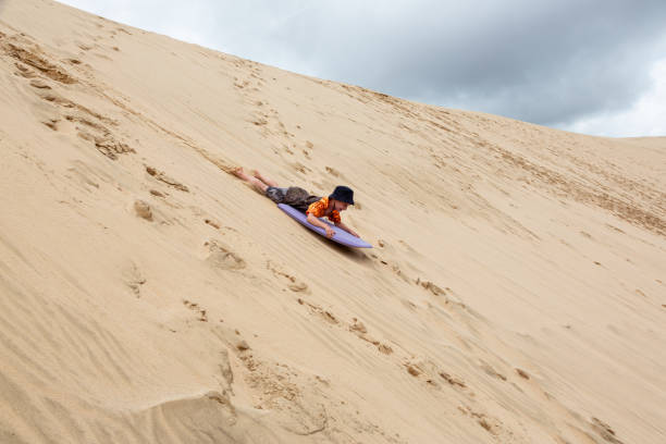 Young boy flying down a sand dune on a board. stock photo