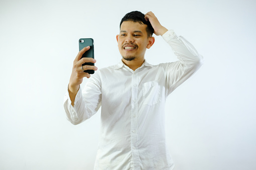 Adult Asian man showing confused expression when looking to his phone