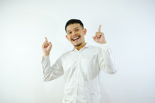 A young asian man pointing something upside with his both hand over white background