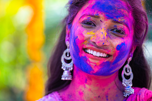 Close up head shot of happy indian girl with colored face during holi festival celebration - concept of enjoyment, happiness and Indian culture