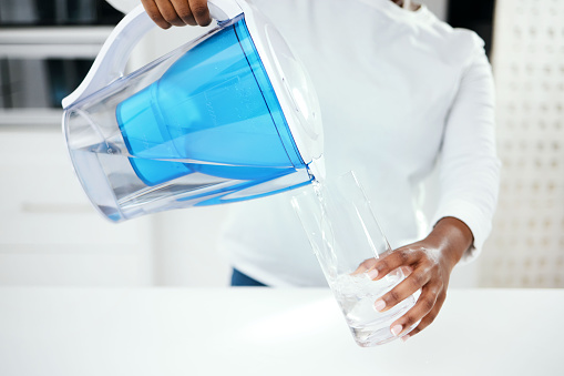 Hands, jug and glass of filter water to refresh with pure liquid hydration at home. Closeup, thirsty person and pouring healthy aqua beverage in container for nutrition, drinking and cold filtration