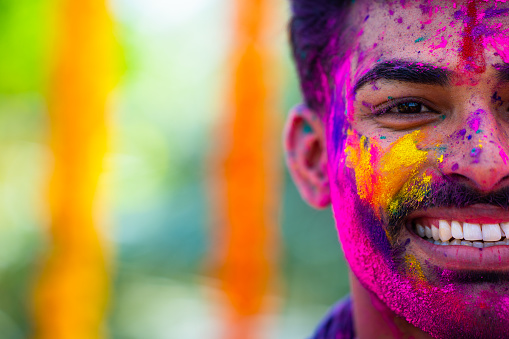 Half face shot of happy smiling indian man with holi color on face showing copy space - concept of happiness, excitement and wellness