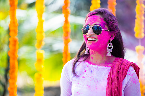 Happy indian young girl with holi colour applied on face during holi festival celebration on flower background - concept of enjoyment, holi celebration and freedom.