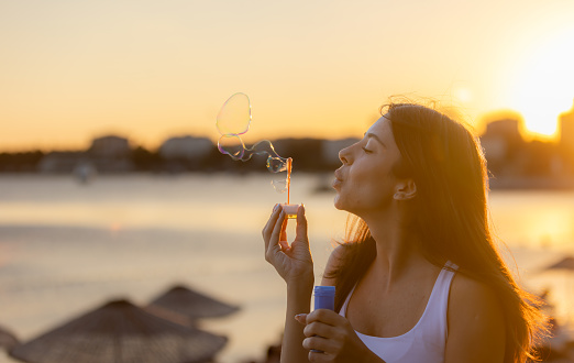 Pretty young woman is blowing bubbles front of cityscape at sunset.