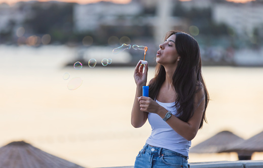 Pretty young woman is blowing bubbles front of cityscape at sunset.