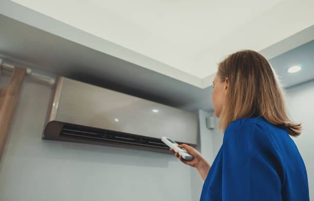 istock Woman holding remote control aimed at the air conditioner. 1560745726