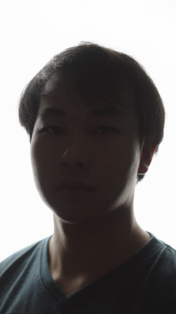 Portrait view of an Asian man turning his face toward the camera, staring straight at it while in deep thought