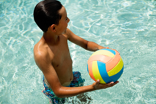 Young boy with ball in swimming pool. Kid is 10 years old. Horizontal waist upoutdoors shot with copy space. This was taken in Florida, USA.