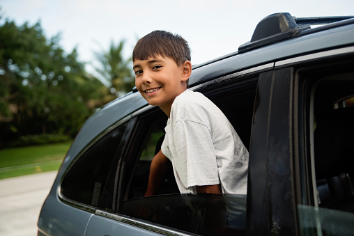 Morning routine for young boy getting in car to go to school. Kid is 10 years old and is looking at the camera with a smile. Horizontal waist up outdoors shot with copy space. This was taken in Florida, USA.
