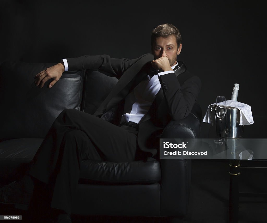 Sexy man in tuxedo waiting for his date Sexy handsome man in tuxedo sitting in the darkness of a nightclub with an unopened bottle of champagne on ice waiting for his date Playboy Stock Photo