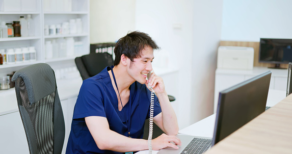 asian happy male nurse is speaking on phone and discussing about work in the hospital nursing station