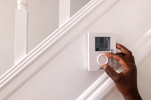 A close-up of an unrecognisable mature male adult's hand adjusting the thermostat at home. The thermostat is located on the staircase.