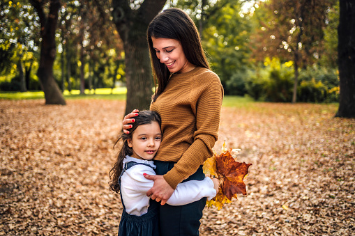 Happy mum and cute daughter hugging during a beautiful autumn day in the park