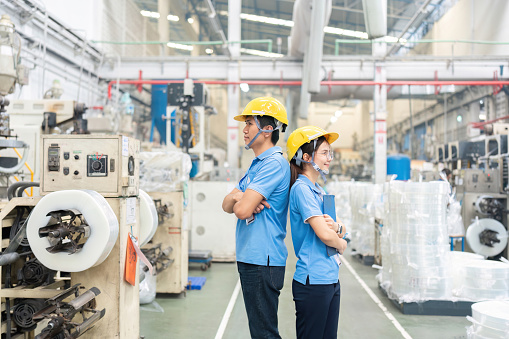 Asian managers and engineers smartly stand back to back in a plastics factory with machines. looking at the destination with hope for future business and projects