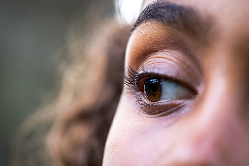 Extreme close-up of a young girl's eye. She is looking away from the camera focusing on her eye. She has a brown iris which are reflecting her surroundings.