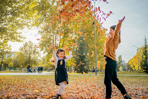 happy mother and  daughter throwing autumn leaves in the air in autumn park