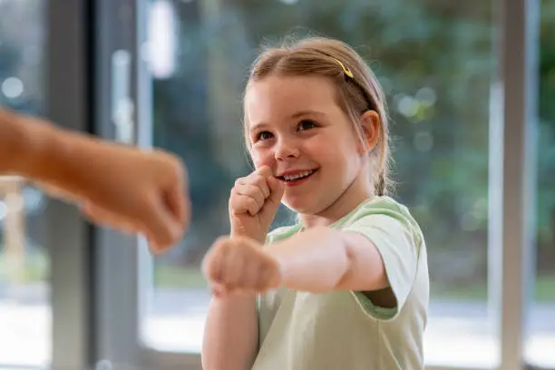 Close-up of a little girl duringa. kickboxing class. She is looking at her unrecognisable opponent with her hands raised into a defensive position and smiling.