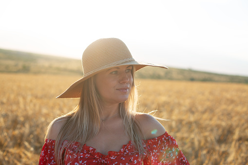 caucasian blonde woman in a red dress and hat on the golden wheat field in sunset light
