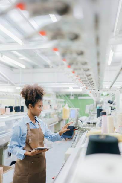 istock American female designer pressing a control panel from a weaving machine. in the sewing industry to produce clothes according to her designs In her hand is a tablet to use. There are threads around. 1560872941