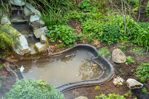 Preformed pond newly inserted into a garden under a waterfall water feature.