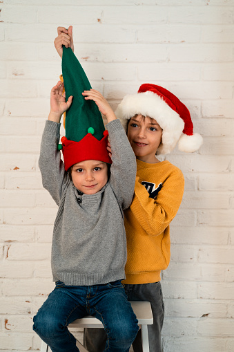 Children  having fun posing against brick white wall with Elf hat  for a Christmas greeting card