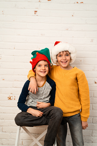 Children posing against brick white wall with Santa and elf hat  for a Christmas greeting card
