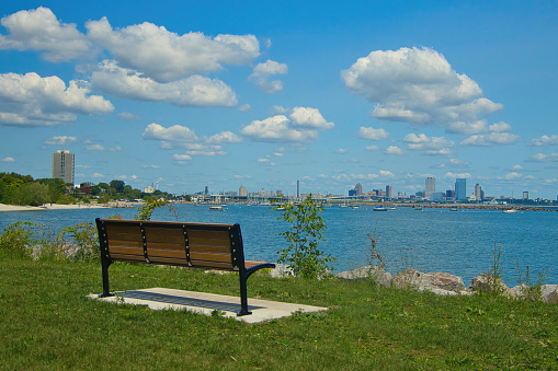 On a partly cloudy summer day, an empty bench faces Downtown Milwaukee as seen from across the Lake Michigan harbor.