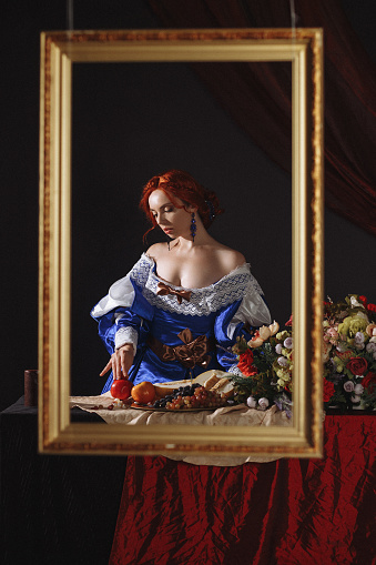 Portrait of a noble lady with fruit in the style of a framed painting. Vintage of a young charming girl in the image of a medieval royal in a renaissance style dress isolated on a dark background.