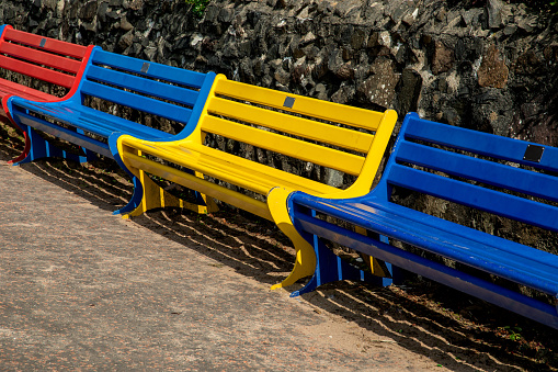 Public benches of assorted colours at a wall at a beachside walkway