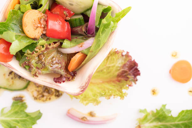 Messy salad with Italian dressing on a white background.  Tomato, red onion, carrot, lettuce, bell pepper, herbs, spices, oil and vinegar.